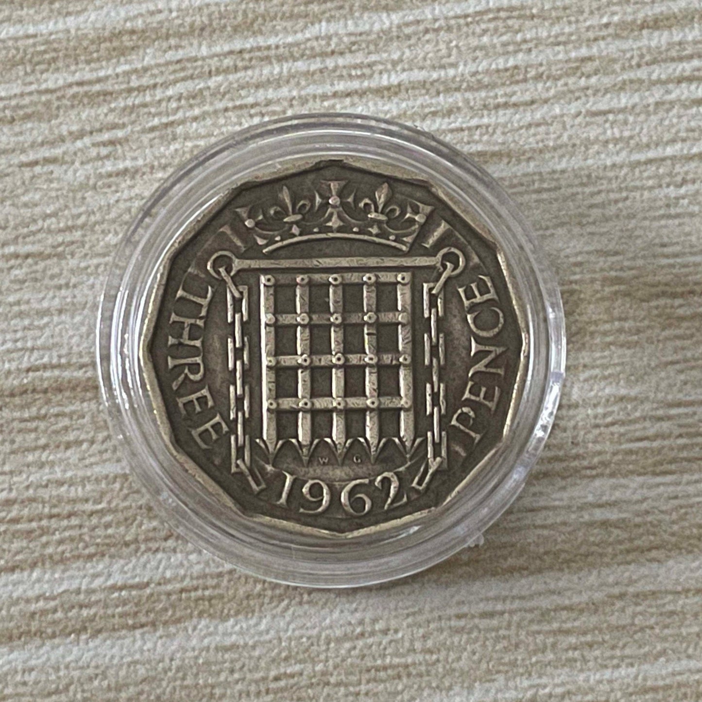 Queen Elizabeth II brass threepence coin in protective capsule, reverse