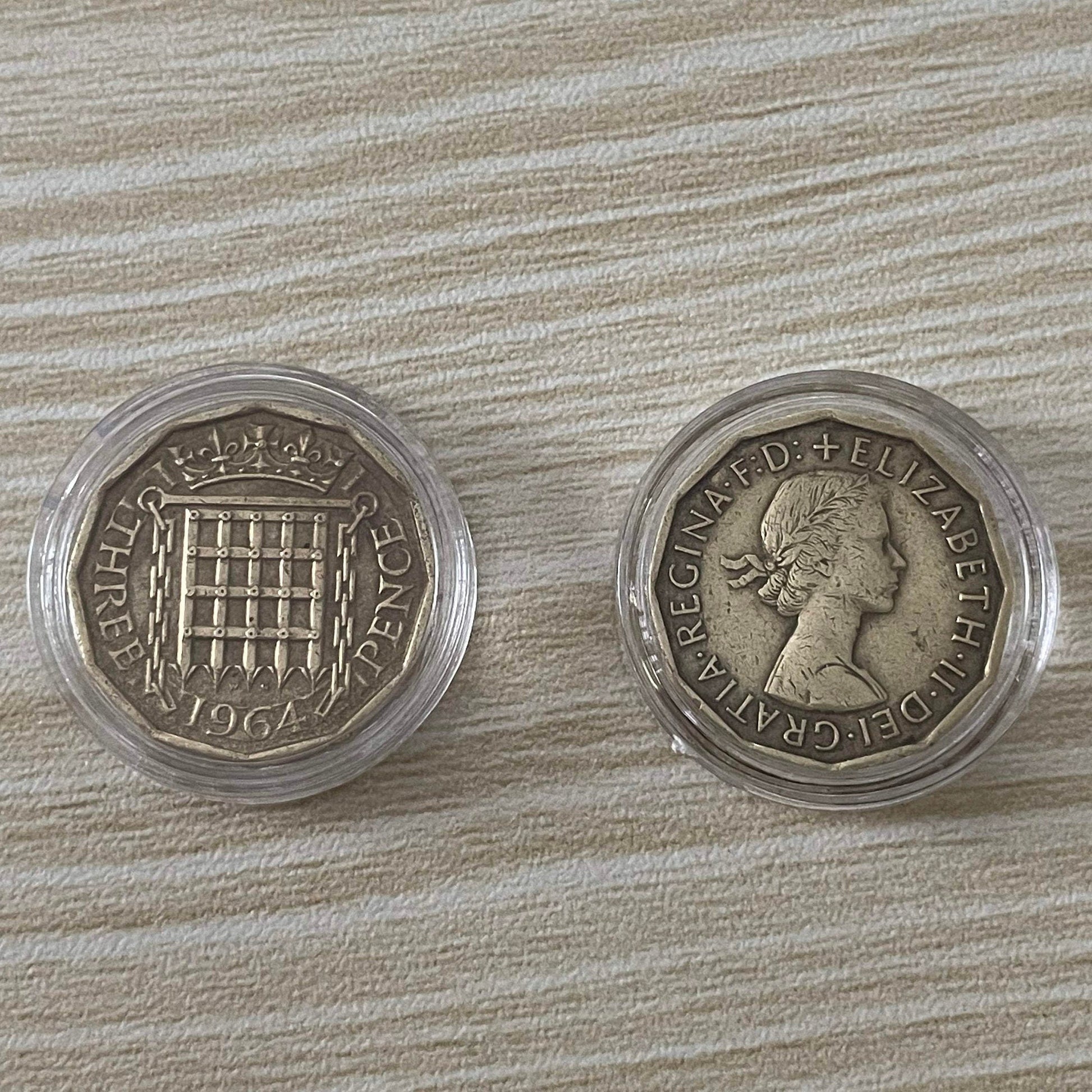 Queen Elizabeth II brass threepence coins in protective capsules, obverse and reverse