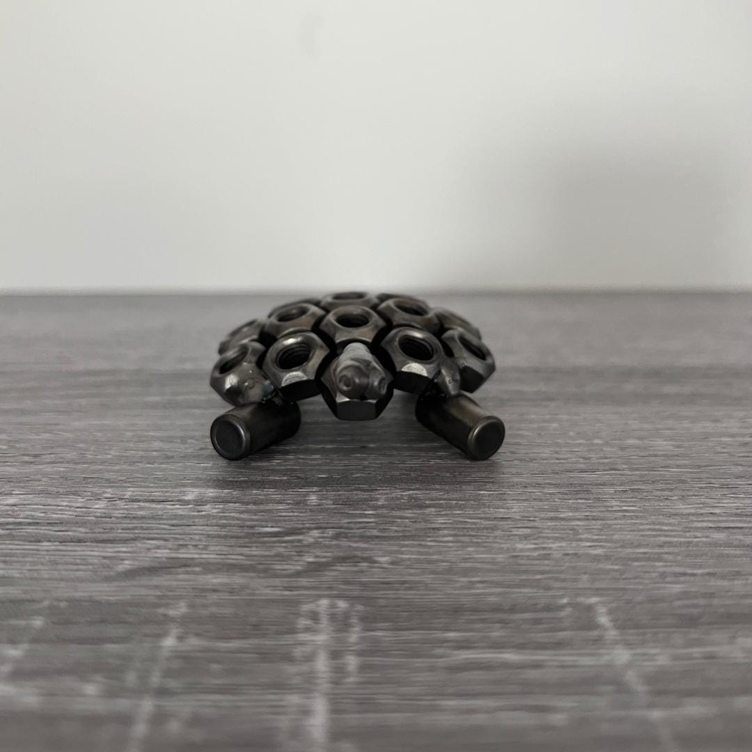 Industrial-style scrap metal tortoise sculpture made from hex nuts and bolts, handmade recycled metal art ornament on wood background, front view