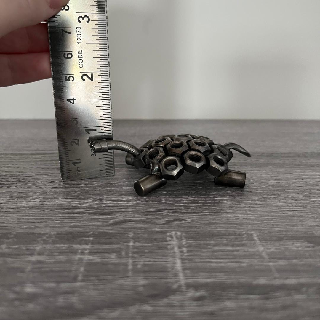 Industrial-style scrap metal tortoise sculpture made from hex nuts and bolts, handmade recycled metal art ornament on wood background, showing height