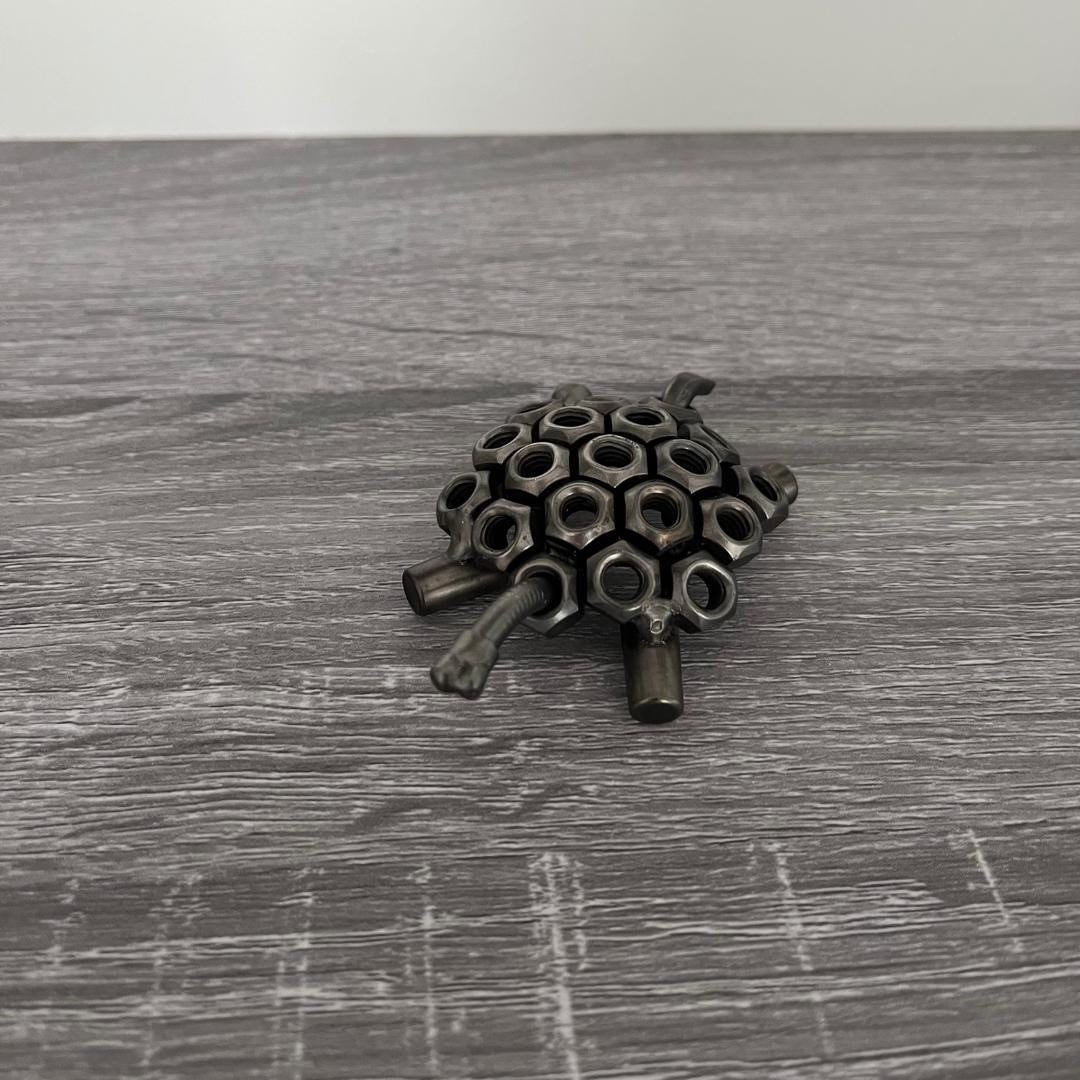 Industrial-style scrap metal tortoise sculpture made from hex nuts and bolts, handmade recycled metal art ornament on wood background