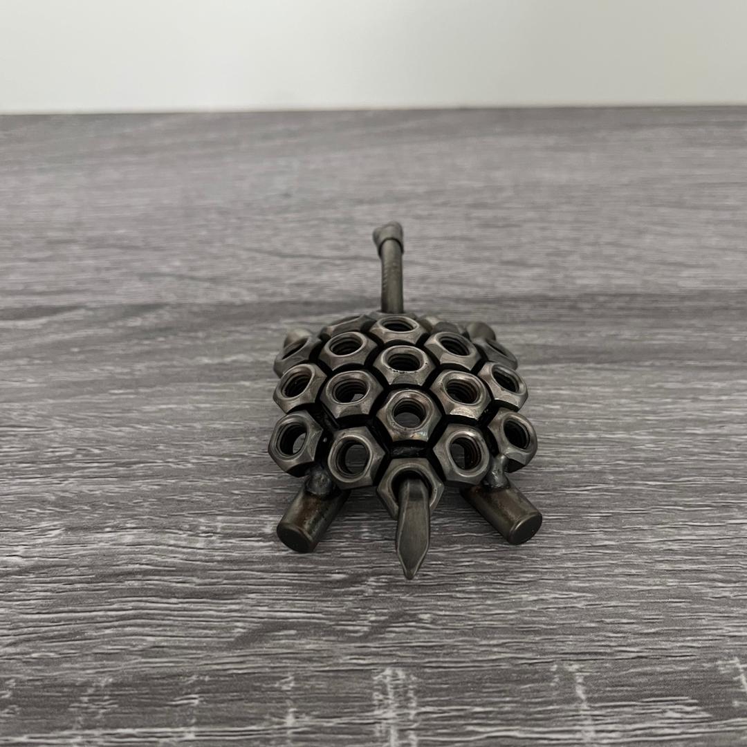 Industrial-style scrap metal tortoise sculpture made from hex nuts and bolts, handmade recycled metal art ornament on wood background, rear view