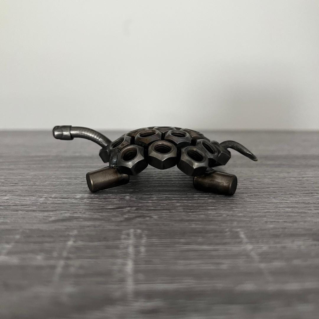 Industrial-style scrap metal tortoise sculpture made from hex nuts and bolts, handmade recycled metal art ornament on wood background, side view